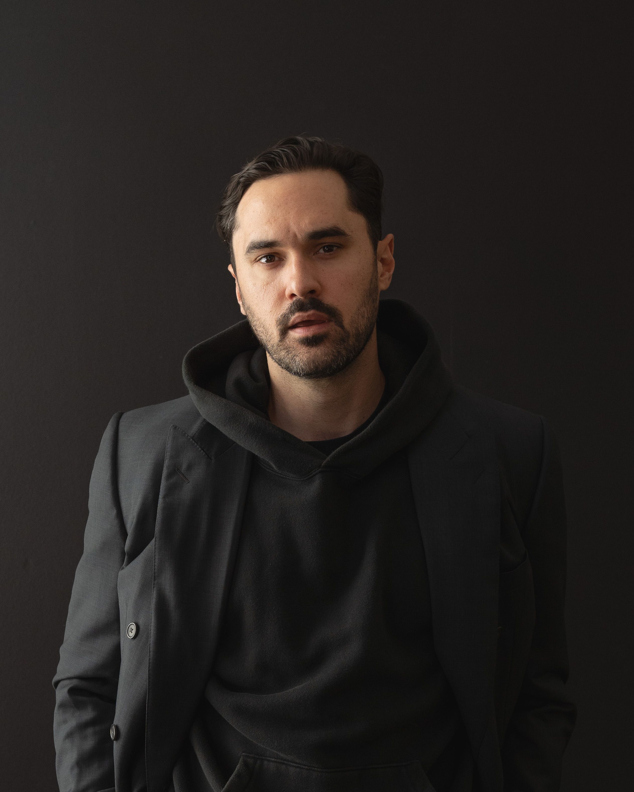 Rob Howe in a black hoodie and blazer against a black backdrop